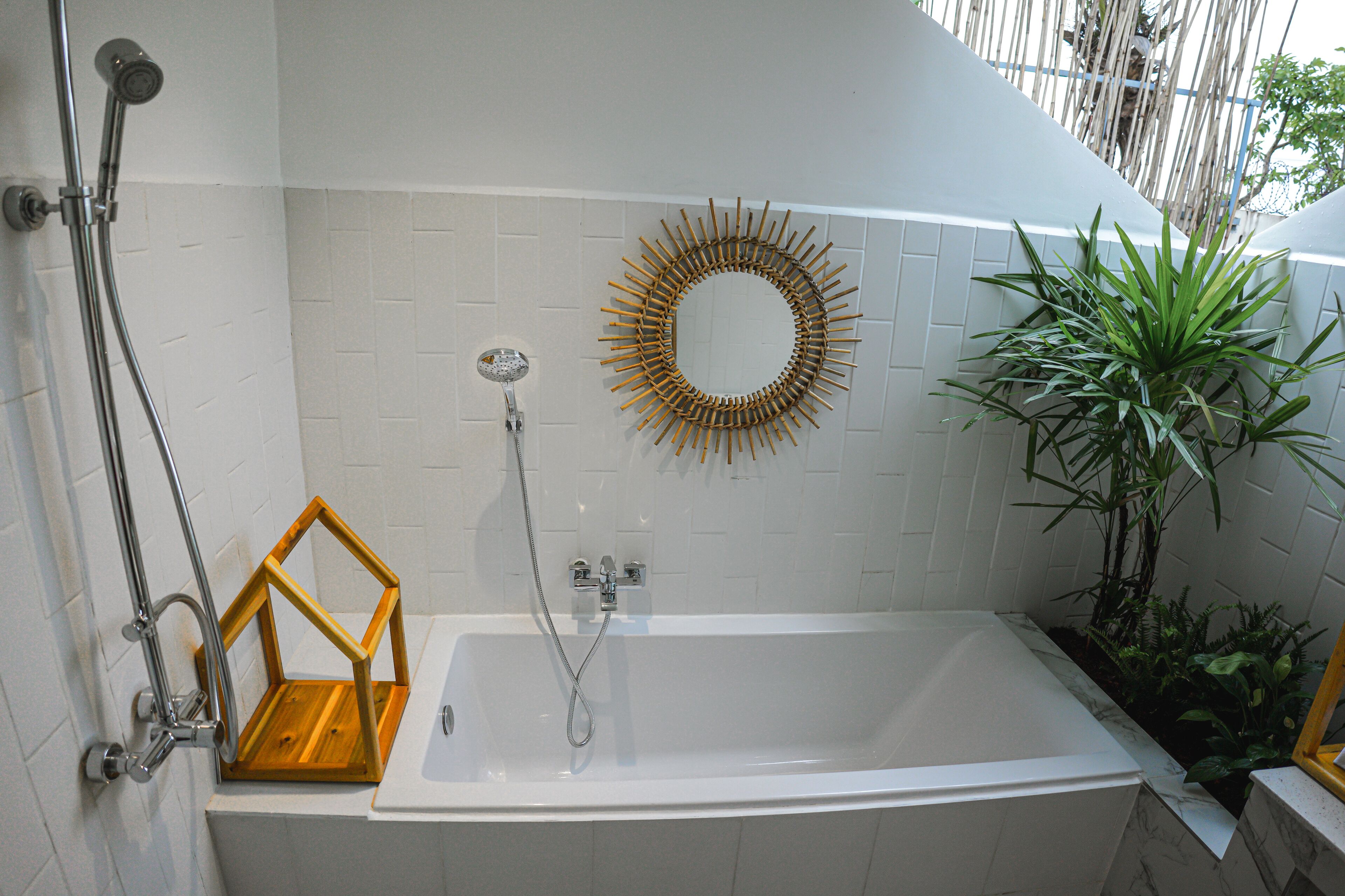 A modern bathroom with a freestanding bathtub, a shower with a handheld showerhead, a wooden geometric shelf, and a decorative sunburst mirror.