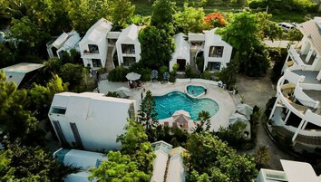 Un moderno resort con varias edificaciones blancas, una piscina central y exuberante follaje.