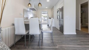 A modern kitchen with white cabinets, stainless steel appliances, and a dining area with white chairs and pendant lights. - Vacation home Aeris by Interhome (Cunit)