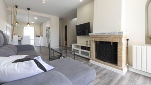 A modern living room with a grey sofa, a fireplace, a TV mounted above it, and a kitchen in the background. - Vacation home Aeris by Interhome (Cunit)