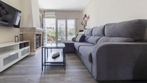 A modern living room with a grey sofa, a flat-screen TV mounted on the wall, a fireplace, and a balcony with a view of greenery. - Vacation home Aeris by Interhome (Cunit)