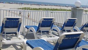 A beachside lounge with blue and white lounge chairs, a white railing, and a view of the beach and ocean. - Beachfront  top flr 1 br condo at Summer Sands (Wildwood)