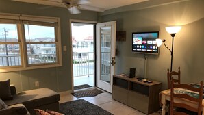 A living room with a sofa, a coffee table, a TV on the wall, a dining table with chairs, and a balcony door. - Beachfront  top flr 1 br condo at Summer Sands (Wildwood)