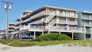 A beachfront hotel with multiple balconies, a parking area, and a sandy beach in the foreground. - Beachfront  top flr 1 br condo at Summer Sands (Wildwood)
