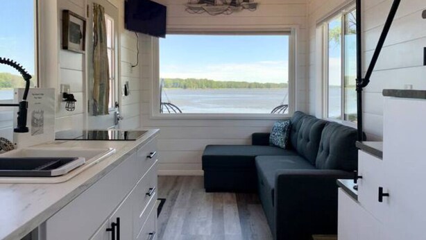 Interior de una cabaña moderna con cocina, zona de estar con vistas a un lago y techo de madera.