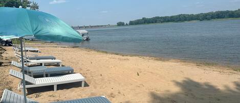 A beach with white lounge chairs and a large umbrella.