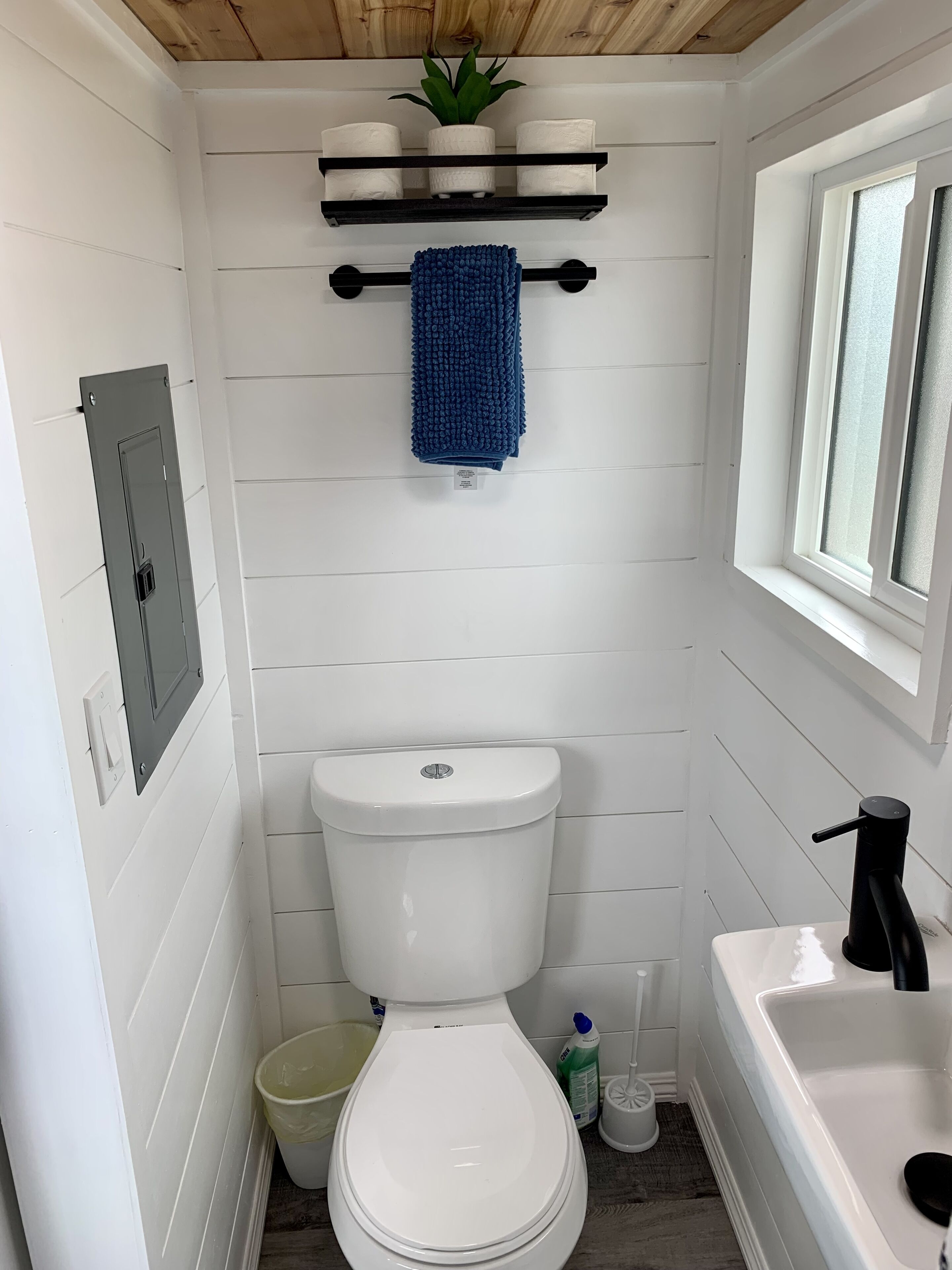 Een kleine badkamer met een wit toilet, een klein wastafeltje en een raam.