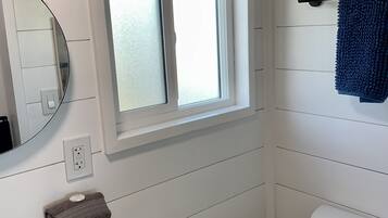 Une salle de bain avec un lavabo blanc, un miroir, une fenêtre, un porte-serviettes et des toilettes.