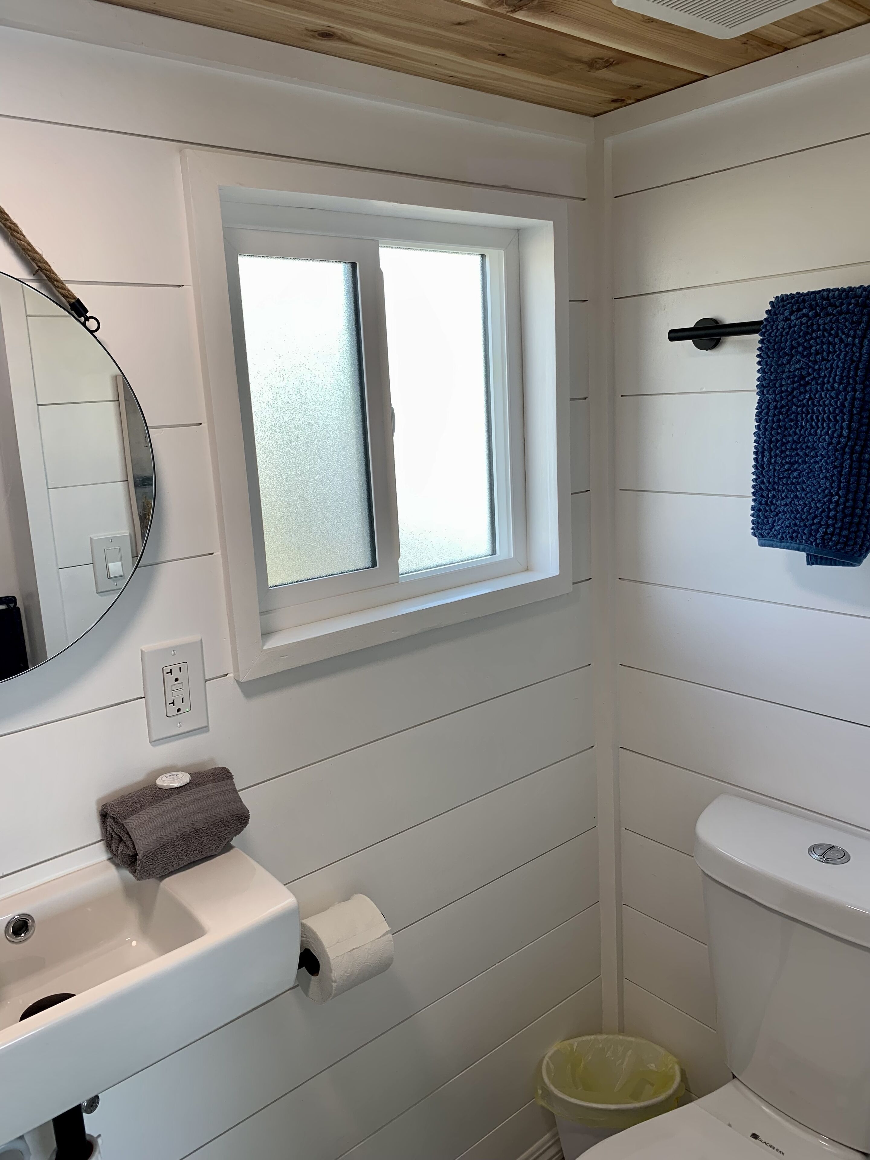 Un baño con lavamanos blanco, espejo, ventana, toallero y inodoro.