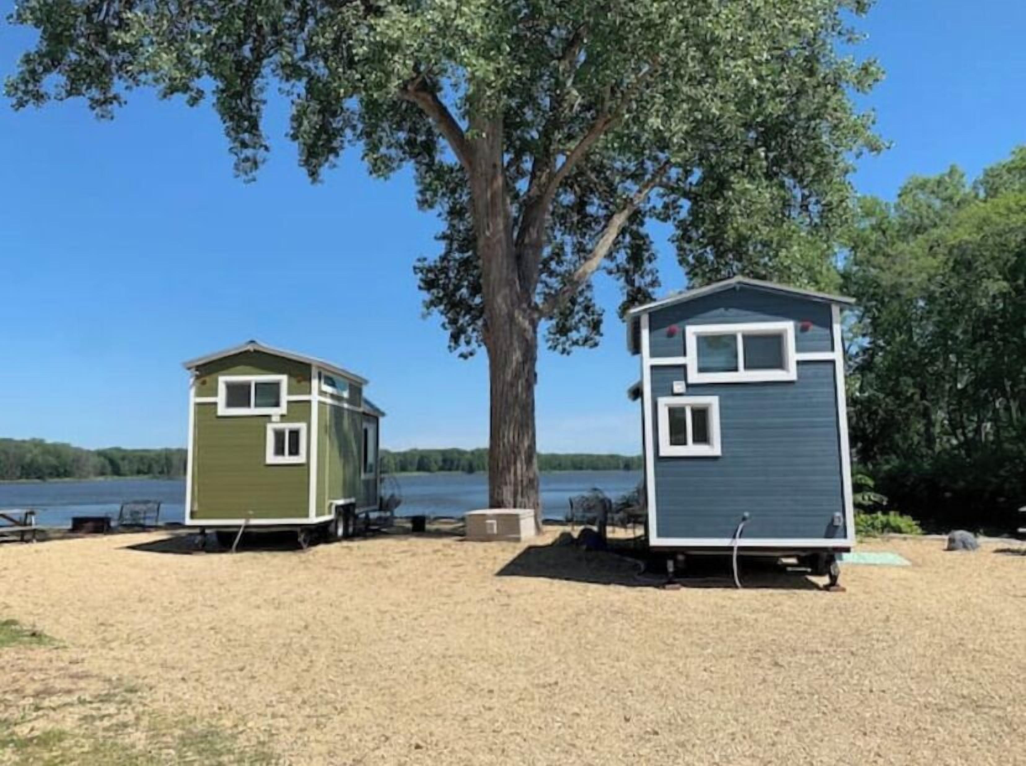 Two small, single-story cabins with a clear view of a lake and trees in the background.