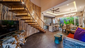 Un salon moderne avec un escalier en bois, un coin repas et une cuisine en arrière-plan.
