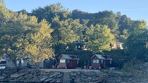 Une propriété au bord du lac comprenant deux petits chalets, une jetée en pierre et une colline boisée.