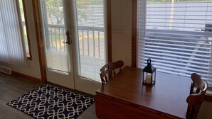 Une pièce comprenant une table à manger en bois, deux chaises, un tapis à motifs et une fenêtre avec des stores.