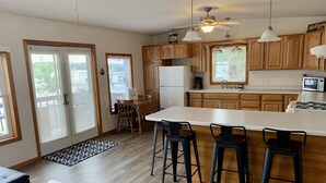 Une cuisine moderne avec des meubles en bois, un grand îlot central doté de tabourets, un réfrigérateur et un four à micro-ondes.