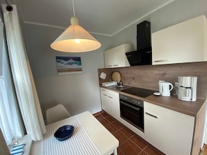 A compact kitchen with a dining area, featuring a stove, sink, and coffee maker.