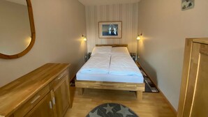 Ein Schlafzimmer mit einem hölzernen Bett, einer Holzkommode, einem runden Spiegel und einer Deckenleuchte.
