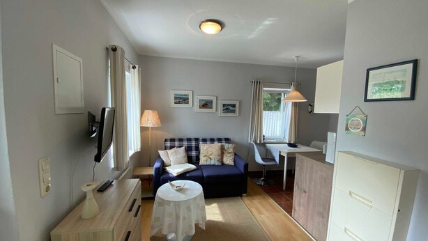Ein kompakter Wohnraum mit Sofa, kleinem Tisch, Schreibtisch und Schrank.