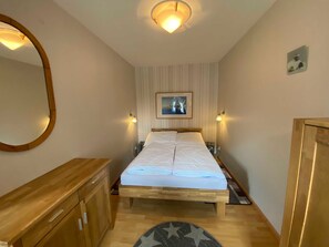 Un dormitorio con una cama de madera, un tocador de madera, un espejo redondo y una lámpara en el techo.