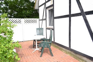 Una veranda esterna con un tavolo bianco e due sedie verdi, una recinzione bianca e un edificio con decorazioni bianco e nero.