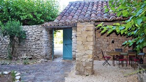 Un edificio de piedra con techo de tejas, una puerta azul y una mesa con sillas.