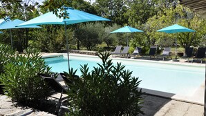 Un área de piscina con sillones de descanso y sombrillas azules.