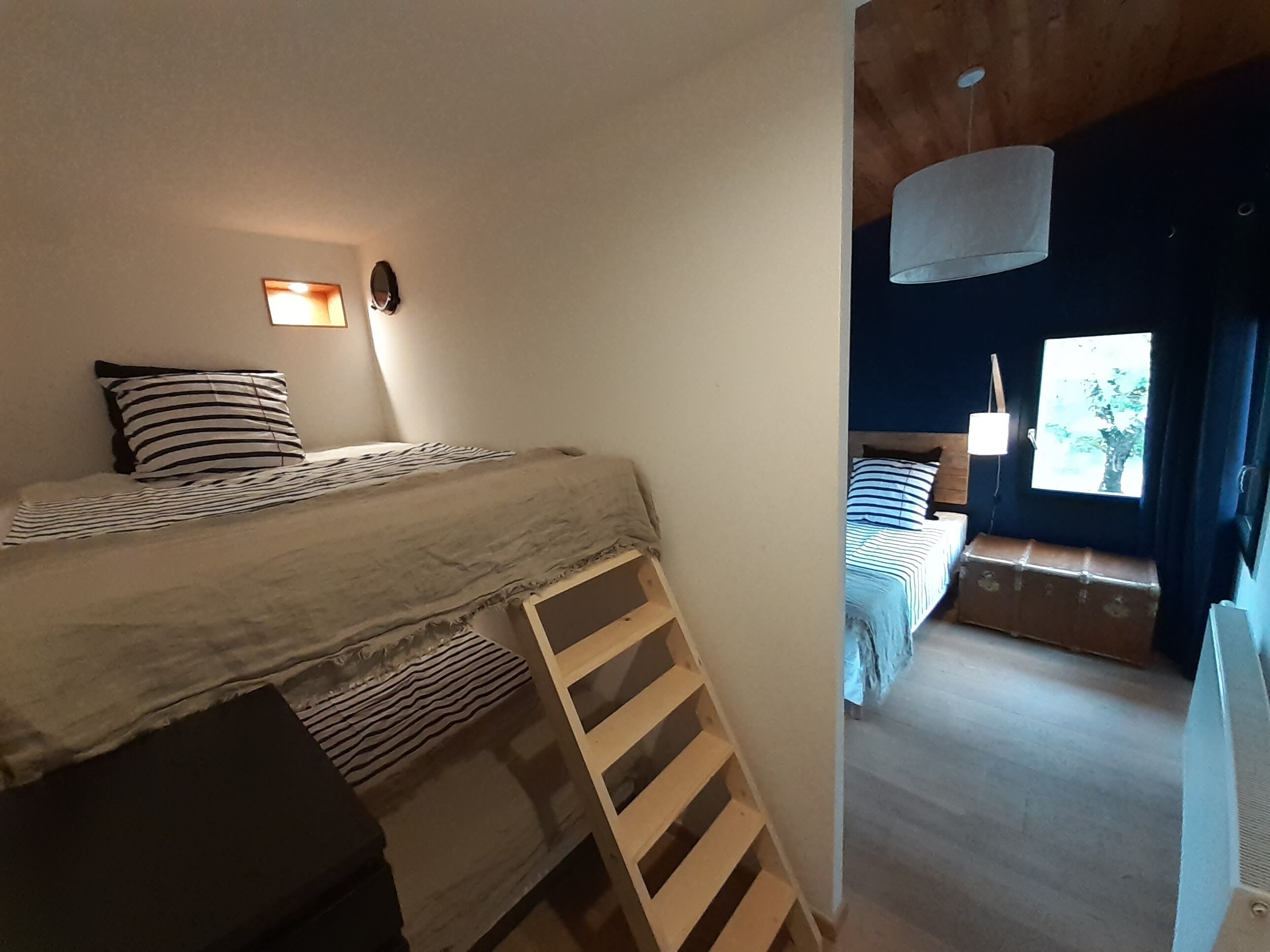 Une chambre confortable avec un lit superposé, un petit bureau et une fenêtre donnant sur les arbres.