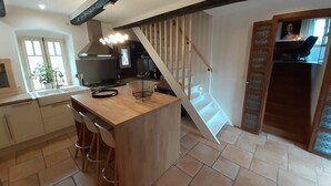 Una cocina con una isla de madera, taburetes de bar, una estufa y una escalera que sube a un altillo.