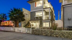 A multi-story residential building with a stone foundation, a white picket fence, and a balcony on the upper level. - Cape-Cod House * 3 Levels+Sky Deck * Beach+Bay Views * Dog OK (San Diego)