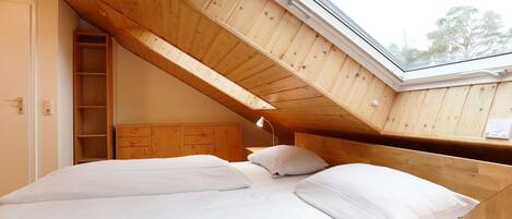 A bedroom with a sloped ceiling, a skylight, a wooden wardrobe, and a bed with white bedding.