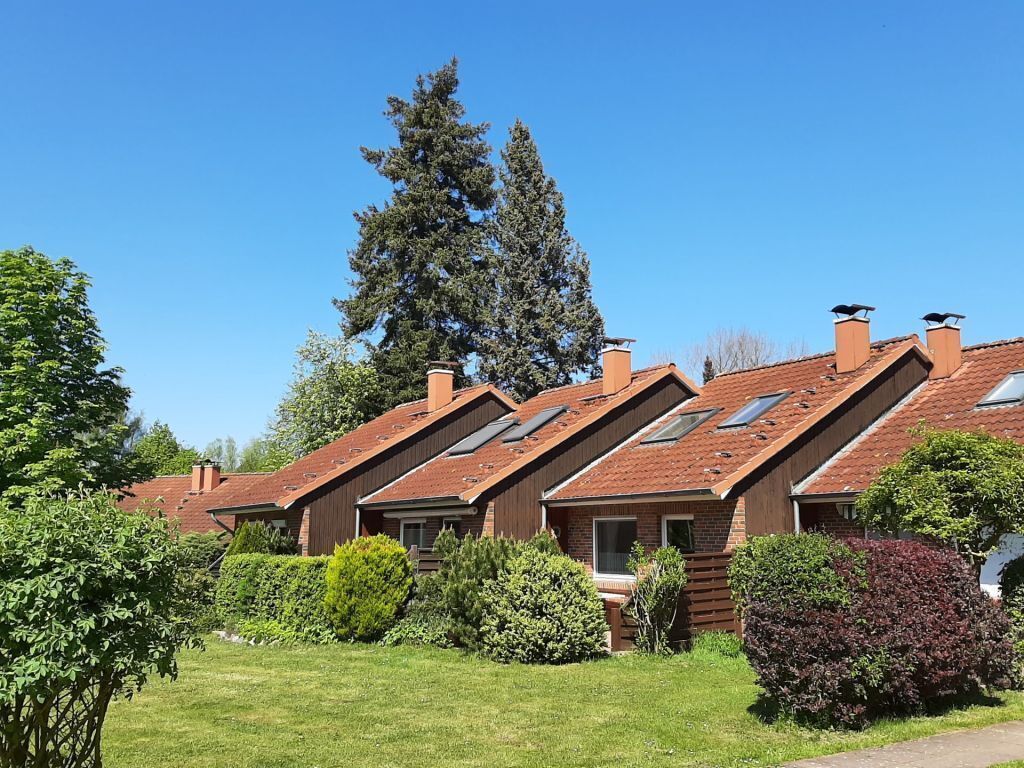 Huse med skrå tage og ovenlys, omgivet af velplejede græsplæner og træer.