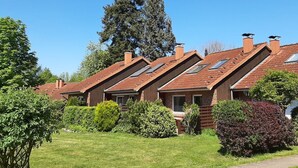 Une rangée de maisons aux toits inclinés et aux lucarnes, entourées de pelouses et d’arbres bien entretenus.