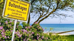 Un panneau jaune avec du texte en allemand, placé sur un fond représentant une plage et des arbres.