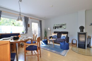 En lys stue med spiseplads, sofaarrangement, pejs og et stort vindue med gardiner.