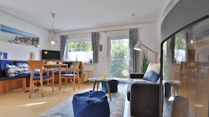 A modern living room with a sofa, chairs, a dining table, and a large window with curtains.