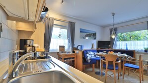 A compact kitchen with a sink, coffee maker, and dining area with a blue sofa and wooden chairs.