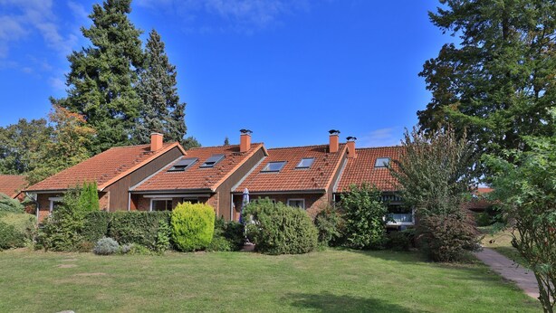 A two-story house with a red-tiled roof, multiple chimneys, and a well-maintained lawn.