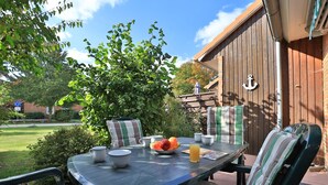 An outdoor patio with a table set for two, featuring a bowl of fruit, a pitcher, and cups.