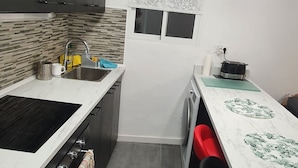A modern kitchen with dark cabinets, a stainless steel sink, a built-in oven, and a dining area with a white countertop and red chairs. - Lighthouseflat next the Marina  (Vilanova i la Geltrú)