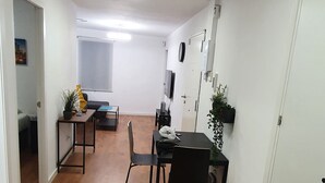 A modern, well-lit room with a wooden floor, a dining table with chairs, a small black table with a plant, and a white door. - Lighthouseflat next the Marina  (Vilanova i la Geltrú)