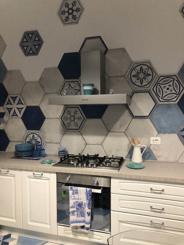 A kitchen with a hexagonal tile backsplash, a gas stove, white cabinets, and a stainless steel range hood. - You can even walk to the beach (San Vincenzo)