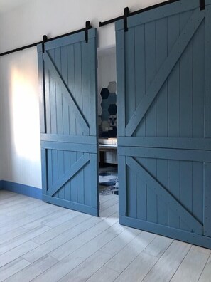 A room with a light wooden floor, a blue sliding barn door, and a hexagonal tile pattern on the wall. - You can even walk to the beach (San Vincenzo)
