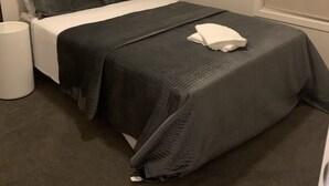 Ein kleines, ordentlich eingerichtetes Schlafzimmer mit einem Einzelbett, einem Nachttisch und einem Mülleimer.