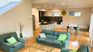Ein modernes Wohnzimmer mit einem Glastisch, zwei grünen Sofas und einem Essbereich mit weißem Tisch und Stühlen.