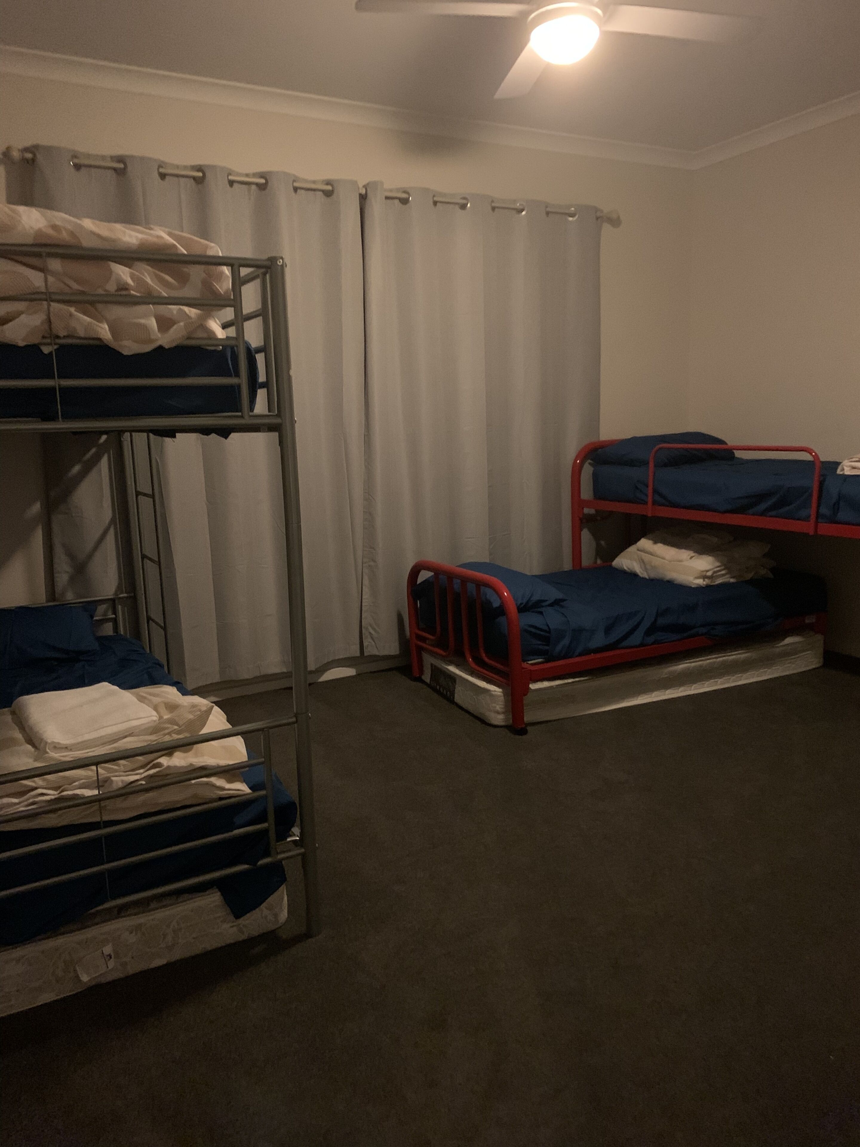 A dormitory room with bunk beds, a ceiling fan, and a window with curtains.