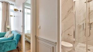 Une salle de bain moderne avec une douche à parois de verre, des toilettes blanches et un canapé turquoise dans la pièce adjacente.