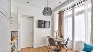 Un salon moderne avec un canapé, une table à manger pour deux personnes et un téléviseur fixé au mur.