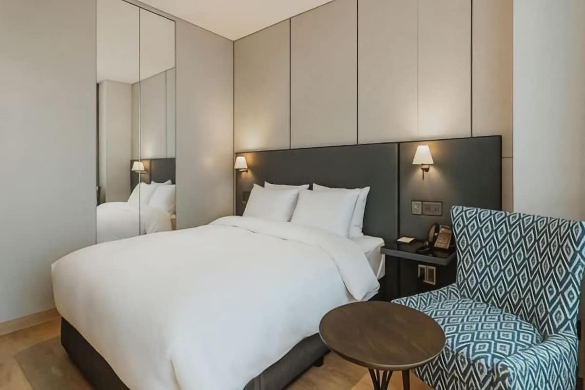 Una camera d'albergo con un letto, un comodino, una lampada e una poltrona con motivo decorativo.