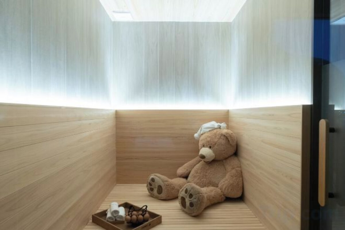 A sauna room with a wooden interior, a large teddy bear, and a tray with bottles.
