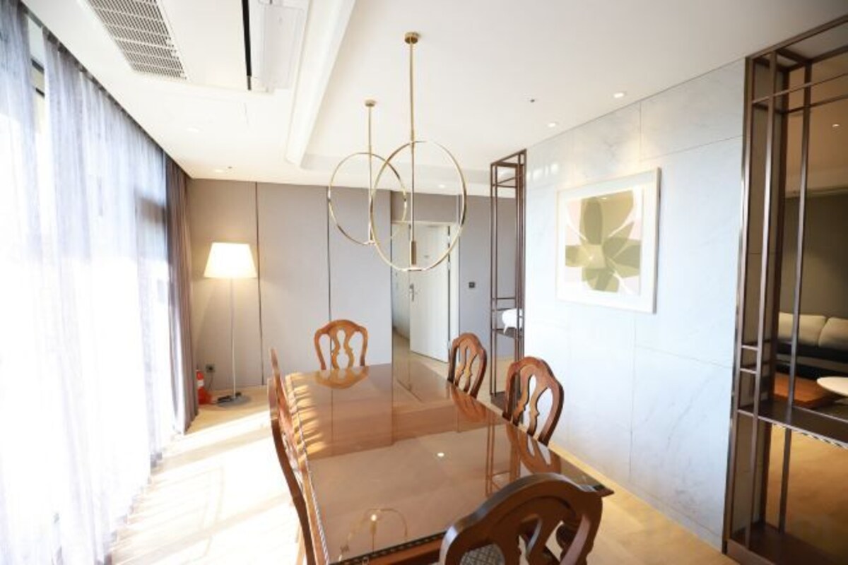 A modern dining area with a long table, chairs, and a chandelier.