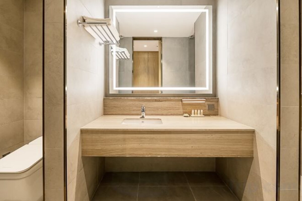 A modern bathroom with a wooden vanity, a mirror with integrated lighting, and a visible shower area.